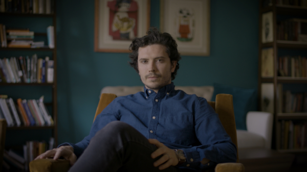 image of filmmaker David Godin. Man in blue button down shirt relaxing in chair with his legs crossed.