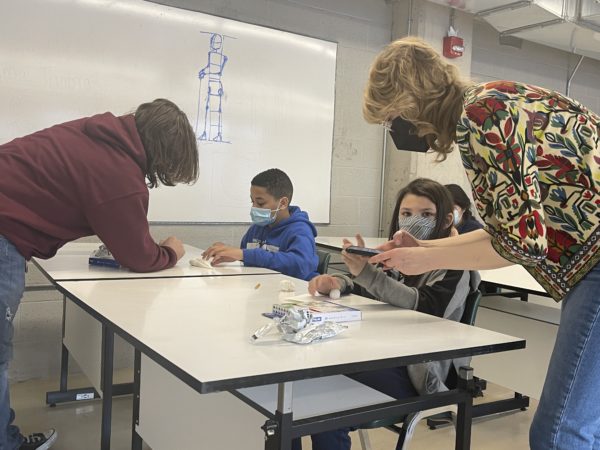 Two adults assist two young students with clay sculpture.