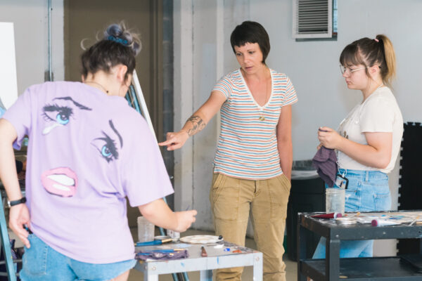 Instructor with short dark hair instructs two student artists.