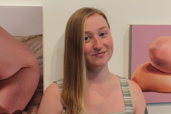 image of woman with long blond hair and slight smile, tank top, posing between two paintings