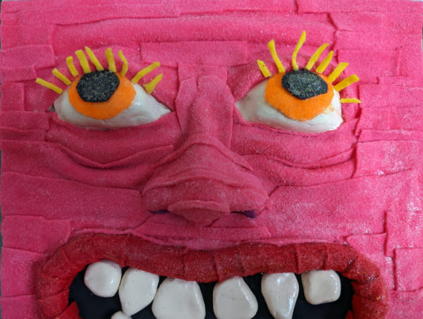 Pink face with yellow eyelashes and an open mouth with teeth