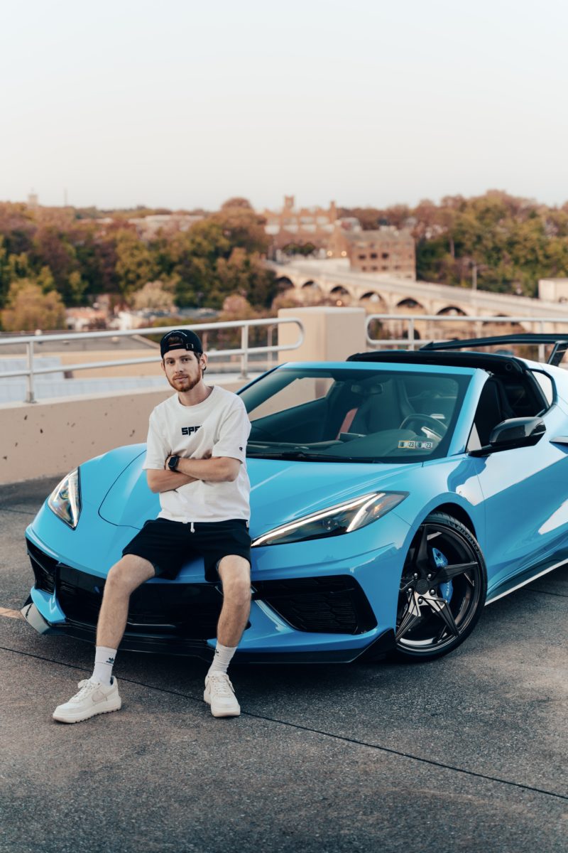 photo of young man leaning against a. bright blue sportscar