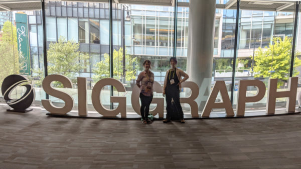 Natasha Warshawsky and Ellie Cochran standing in front of giant SIGGRAPH letters.