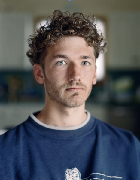 headshot of curly haired young man in blue crew neck shirt.