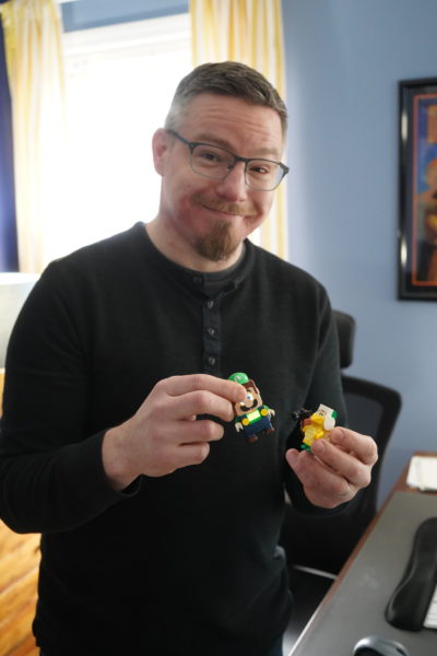 Man with beard in long sleeve black shirt holding Super Mario toys. 