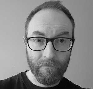 black and white photo of bearded man wearing eyeglasses and dark shirt