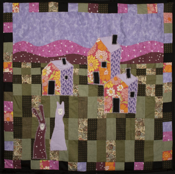 Brightly colored quilt with three patchwork houses in the middle and two bunnies in the lower left corner