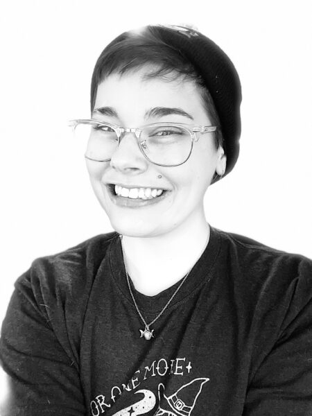 Black and White photo of Jen Sarkisian in a dark colored beanie and glasses. Jen is smiling and wearing a necklace.