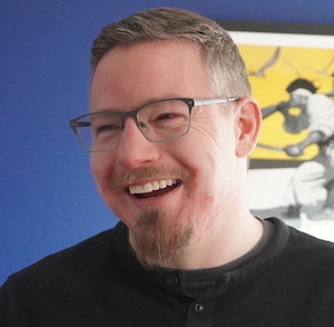 Man with glasses and black crewneck smiling.