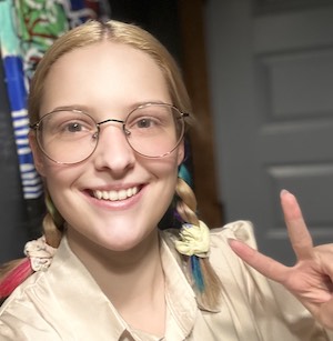 young woman with multicolored pigtails flashing the peace sign and smiling, wearing glasses