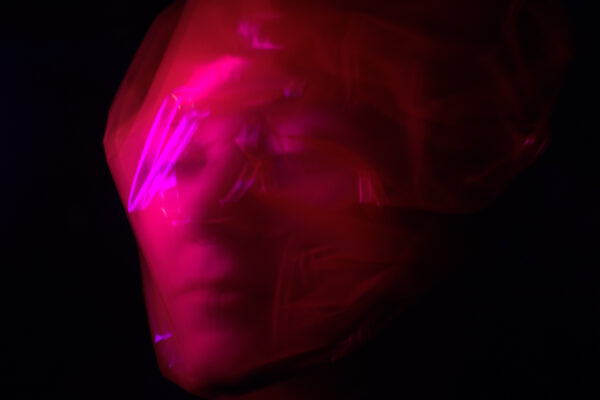 Face wrapped in pink and red emerging from a black background.