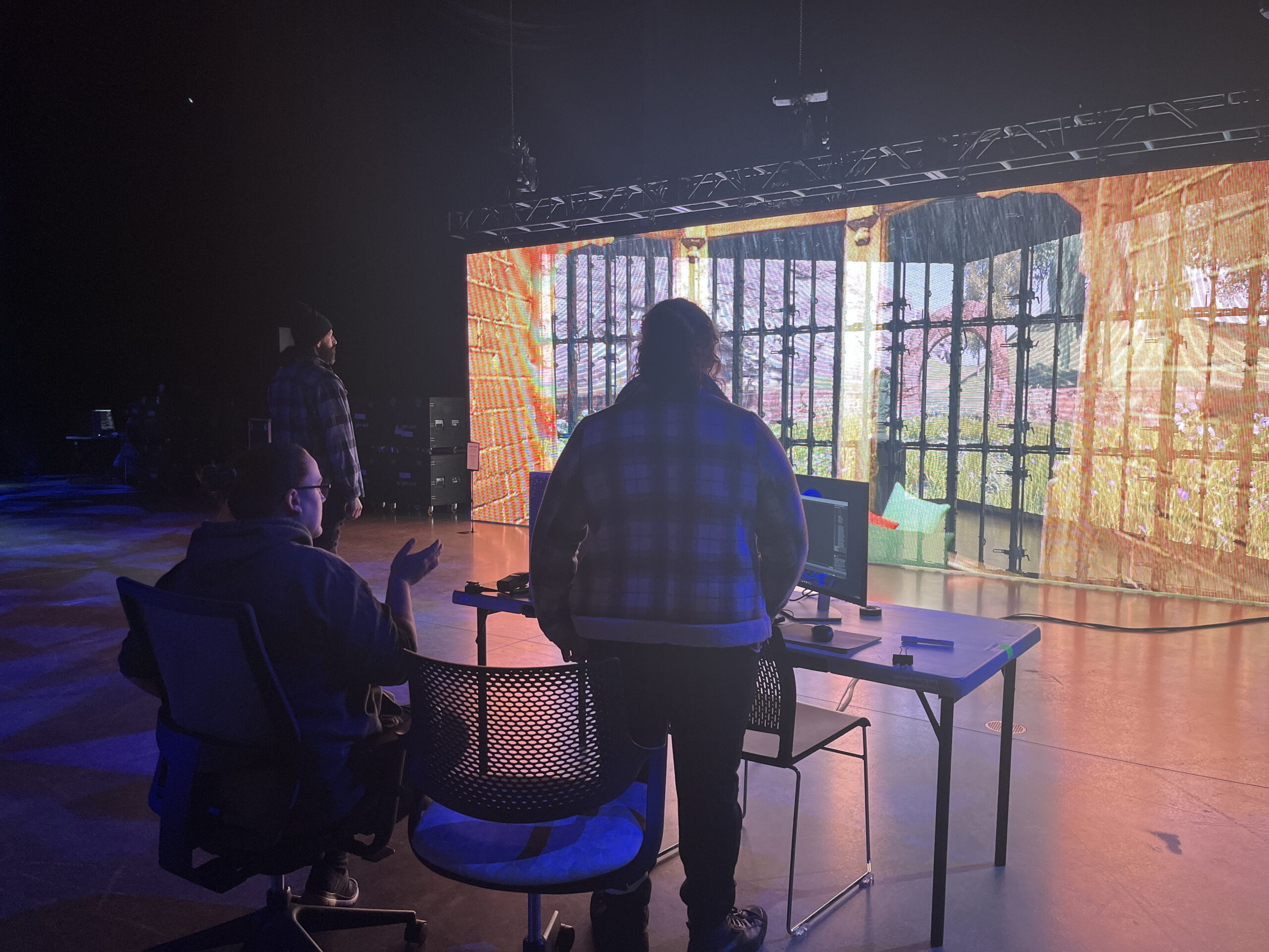 Students work at a lineup of computers set against a wall glowing in the dark.k 