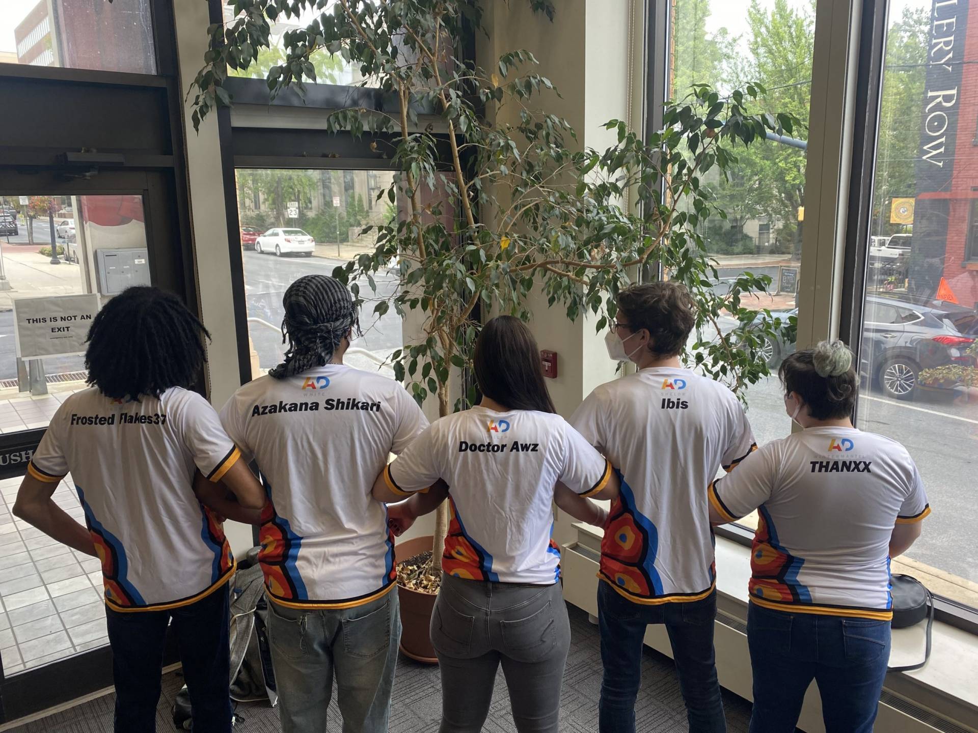 five members in team jerseys link arms; photo from behind. 